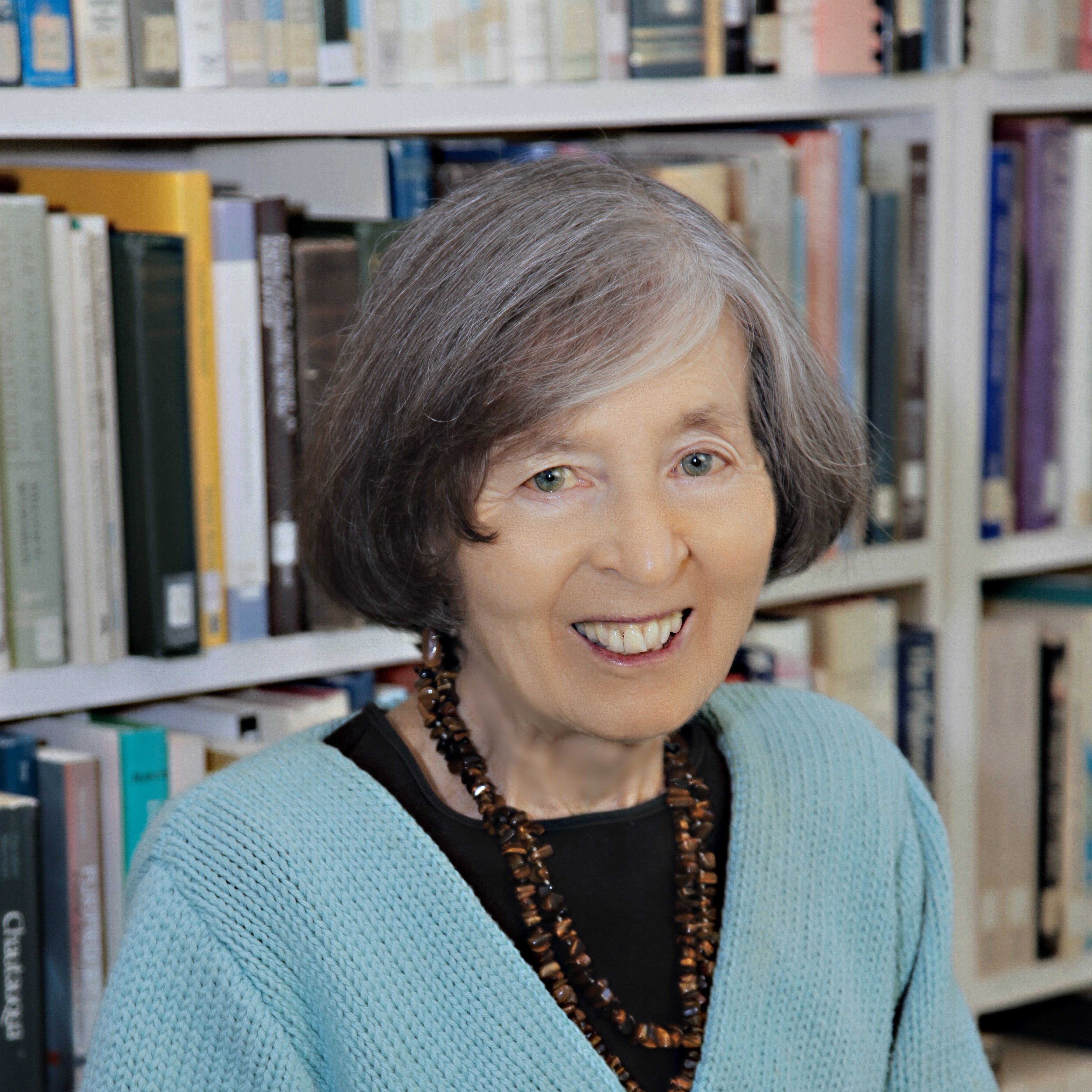 Catherine Albanese in a blue sweater, black shirt, short hair with a bookshelf in the background