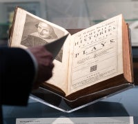 A close-up of an original Fourth Folio (1685), opened to its ornate title page and resting in a glass display case. The book is on loan from Sara Miller McCune for the Infinite Variety exhibition.