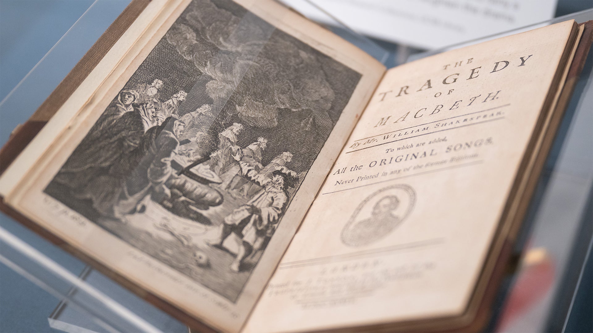 A close-up of a 1734 J. Tonson edition of Macbeth in a glass display case. The book is opened to its ornate title page for the Infinite Variety exhibition.